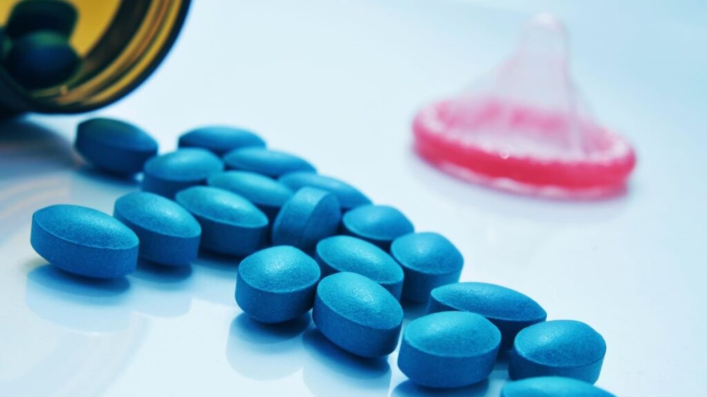 Blue pills for erectile dysfunction and a pink condom on a light blue background