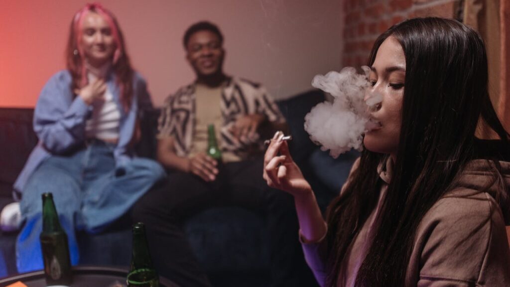 a woman in a hoodie smokes cannabis among partygoers with alcohol