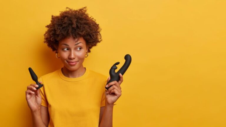 Pretty-woman-holding-two-anal-sex-toys-against-a-yellow-background