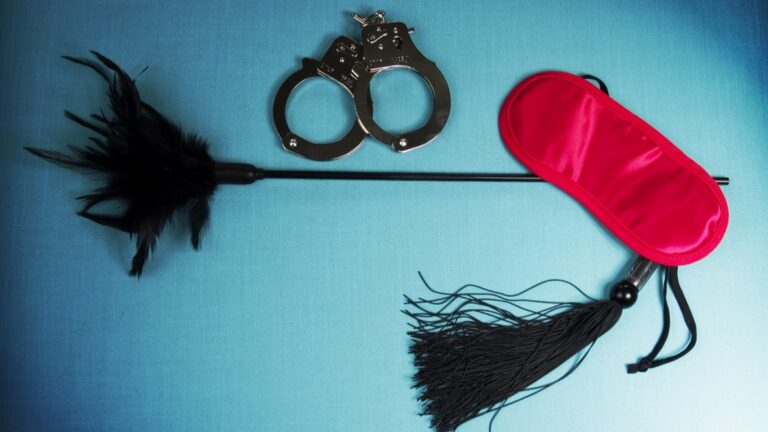 pink blindfold a black flogger and handcuffs on a turquoise background