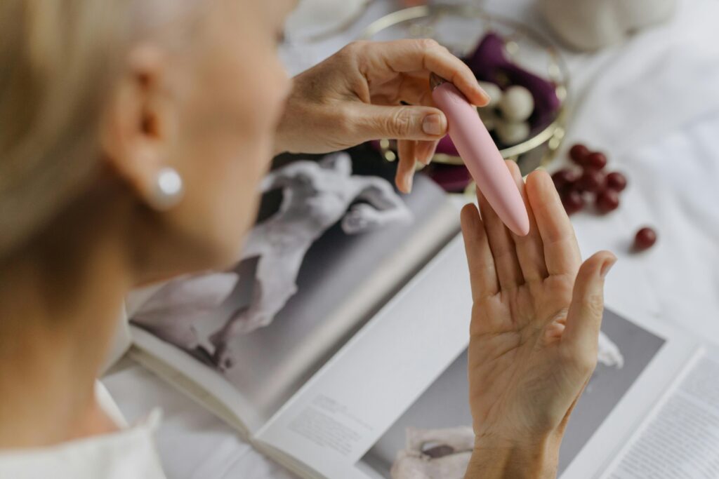 An older white woman examining a pink small vibrator. 