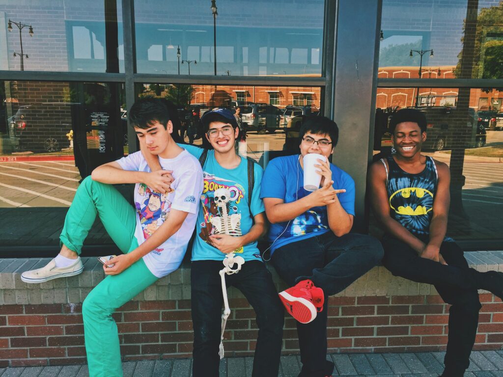 A group of teenage boys are sitting on a wall ledge in front of a large window. 