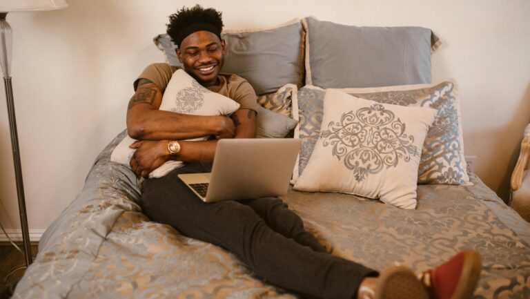 man sitting on bed having a video call on laptop while snuggling a pillow