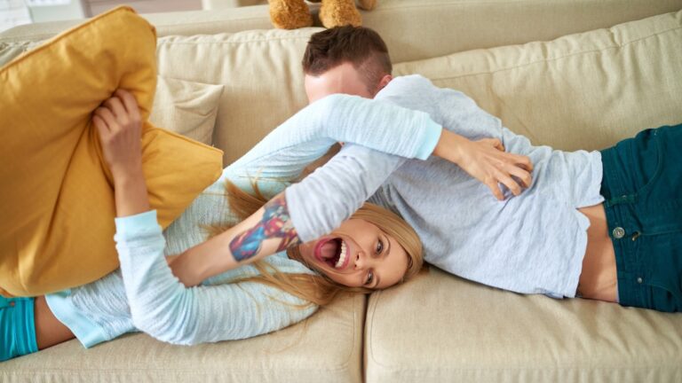 Young white couple tickling each other on a couch