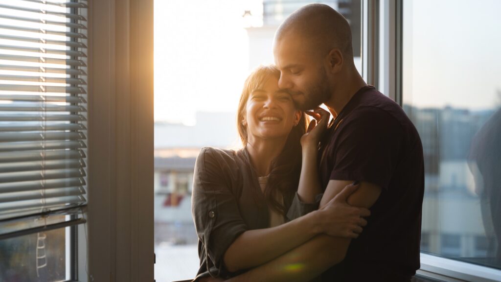 Couple holding each other giving affectionate touch by dim window