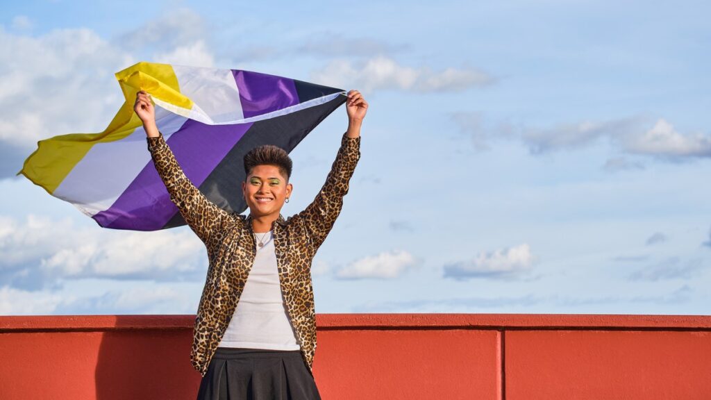 Asian nonbinary person holding non binary flag