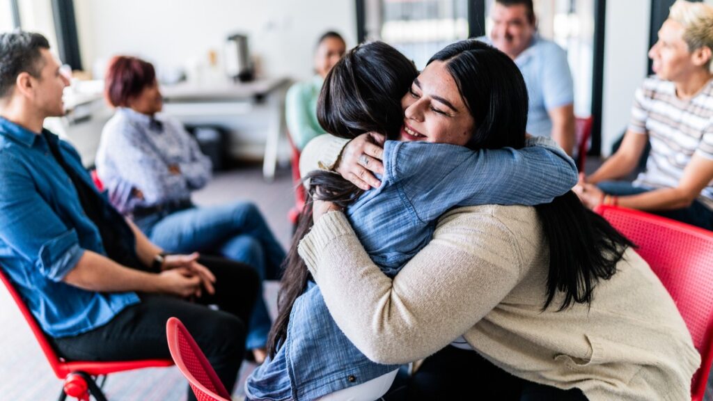 Two adult women embracing in a group sex therapy for couples