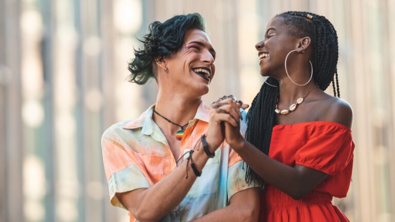 Young couple representing gender and racial diversity hold hands and smile at each other.