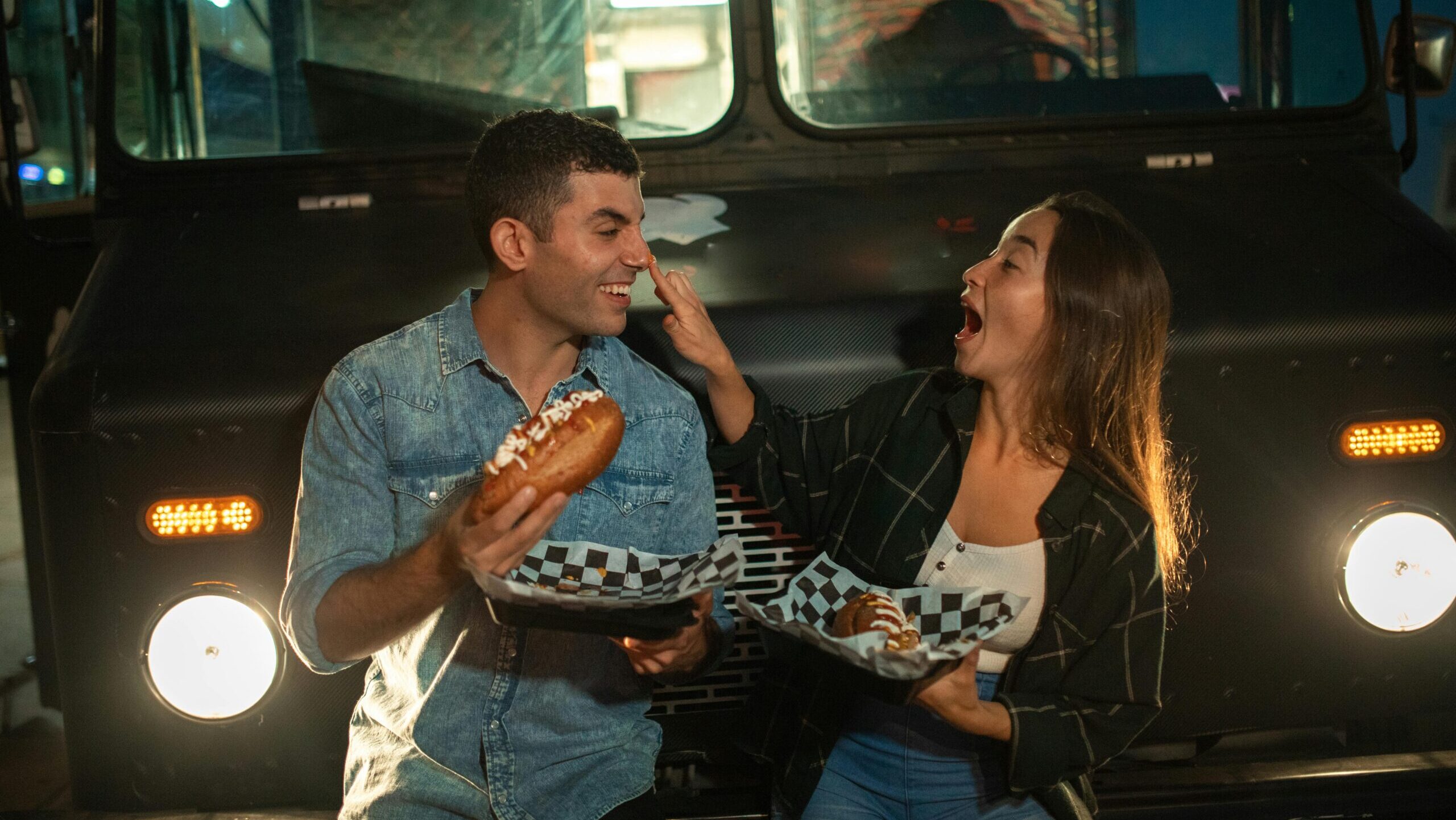 couple eating in front of a food truck and being playful.