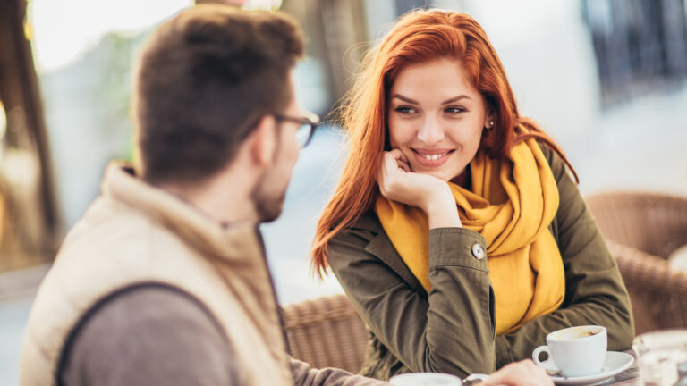 Attractive millennial couple in love sitting at the cafe table outdoors, drinking coffee